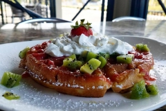 Waffle with  strawberry  and whip cream on top with kiwi fruit and powdered sugar